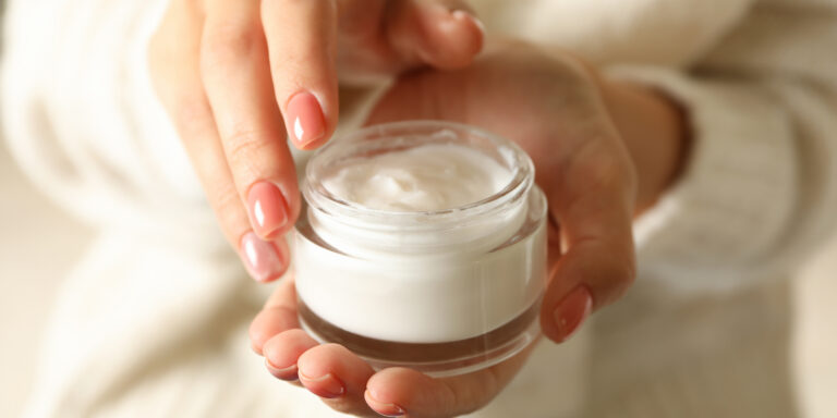 Woman in sweater with pink manicure hold jar of cosmetic cream